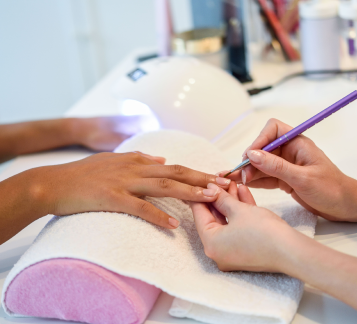 close de uma esteticista pintando as unhas de uma mulher com um pincel em um salão de beleza